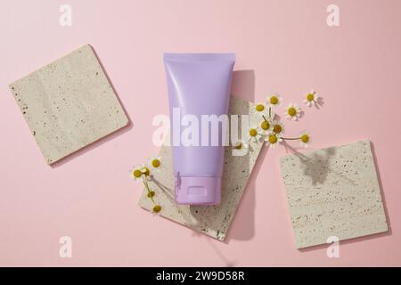 Bouteille en plastique de crème hydratante ou nettoyant pour le visage avec des fleurs de chamomilla et des briques grises décorées sur fond rose. Vue de dessus, étiquette vierge pour Banque D'Images