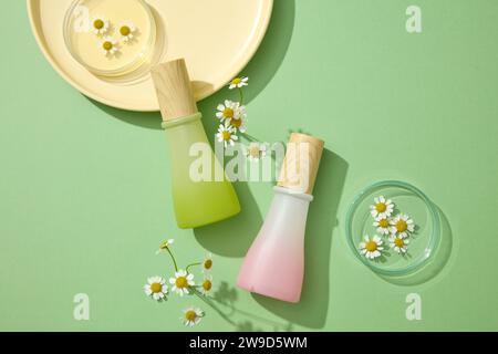 Sur le fond vert, deux bouteilles en verre exposées avec des fleurs de chamomilla fraîches et des plats jaunes. Flacons de maquette pour emballage design. Ext. Naturelle Banque D'Images