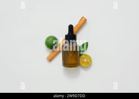 Un flacon compte-gouttes ambré décoré avec des ingrédients pour les huiles essentielles naturelles sur fond blanc. Le citron, le kumquat et la cannelle sont tous des huiles essentielles Banque D'Images