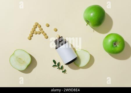 Une bouteille ambrée avec une étiquette blanche décorée de pommes vertes et de pilules disposées en forme de A. Les pommes vertes contiennent beaucoup de vitamine A qui aide im Banque D'Images