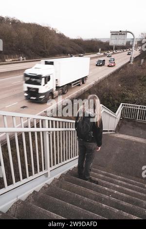 Une femme dans un petit sac à dos regarde la circulation sur la M25 depuis un escalier sur une passerelle dans le nord de Londres Angleterre Royaume-Uni Banque D'Images