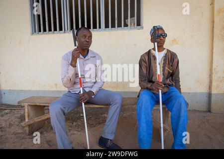 Deux amis aveugles reposent assis sur une plate-forme en bois tenant leurs cannes blanches. Banque D'Images