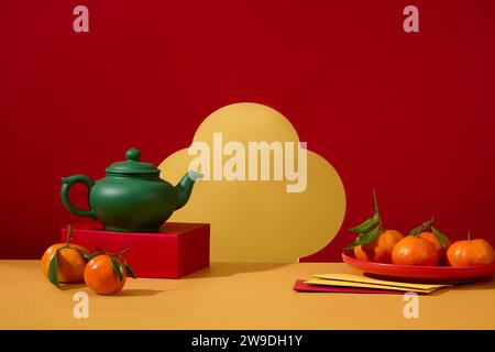 Théière verte posée sur un podium, exposée avec un plat de mandarines et des enveloppes. Les Chinois considèrent le nouvel an traditionnel comme la plus grande holida Banque D'Images