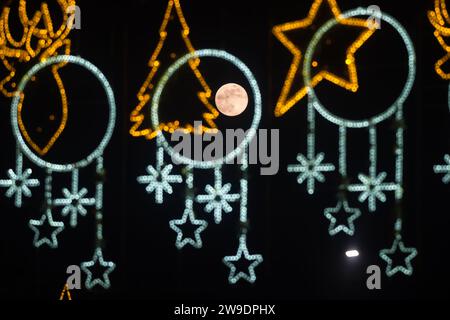 Malaga, Espagne. 26 décembre 2023. La pleine lune de décembre, connue sous le nom de «lune froide», est vue sur le ciel entre les décorations lumineuses de Noël. En décembre a lieu la dernière pleine lune de l'année et la première de l'hiver, appelée la lune froide en raison des températures froides de l'hiver dans l'hémisphère nord. Crédit : SOPA Images Limited/Alamy Live News Banque D'Images