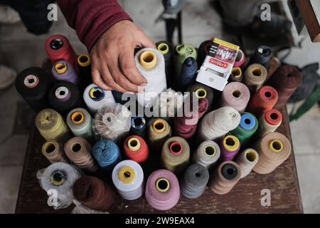 Un tailleur palestinien nommé Abu Adam Dolah utilise une machine à coudre pédalée qu’il a développée en raison d’une pénurie d’électricité Un tailleur palestinien nommé Abu Adam Dolah utilise une machine à coudre pédalée qu’il a développée en raison d’une pénurie d’électricité alors qu’Israël continue de bloquer l’électricité à Rafah, Gaza, le 27 décembre 2023. Gashda a attaché des pédales de vélo à sa machine à coudre d'une manière qui lui permet d'utiliser la machine sans électricité. Photo de Bashar Taleb apaimages Rafah bande de Gaza territoire palestinien 271223 Rafah BT 0014 Copyright : xapaimagesxBasharxTalebxapaimagesx Banque D'Images