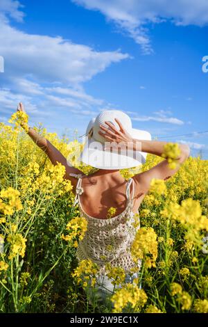 touriste féminine avec un chapeau marchant à travers le champ de floraison jaune au printemps Banque D'Images