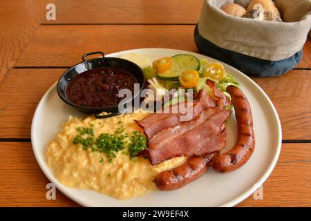 Petit-déjeuner traditionnel typiquement polonais composé de bacon, saucisses, œufs brouillés, salade fraîche, confiture et beurre servi avec du pain dans un restaurant Banque D'Images