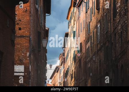 Un ciel sombre de mauvaise humeur au-dessus de bâtiments résidentiels colorés le long d'une rue pittoresque et étroite dans la vieille ville toscane historique de Sienne, Toscane, Italie. Banque D'Images