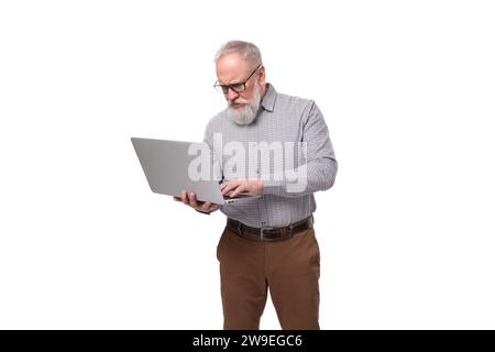 homme d'affaires mature aux cheveux gris réussi avec une barbe et une moustache dans une chemise et un pantalon tient un ordinateur portable Banque D'Images