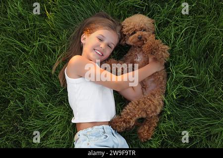 Belle fille avec chien mignon Maltipoo sur pelouse verte à l'extérieur, vue de dessus Banque D'Images