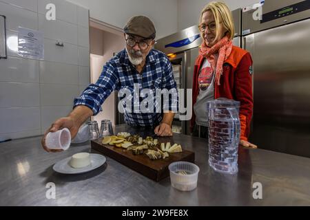 Le fermier de la ferme Ta Zeppi à Siġġiewi, à Malte, présente à la journaliste Angela Berg une planche en bois de fromages ġbejna variés, dont une rondelle recouverte d'herbes, dans sa boutique de ferme. Banque D'Images