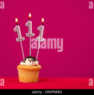 Gâteau d'anniversaire avec bougie numéro 111 - fond mousseux rouge rhodamine Banque D'Images