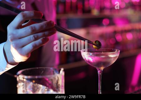 Barman ajoutant des olives dans le cocktail Martini au bar, gros plan Banque D'Images