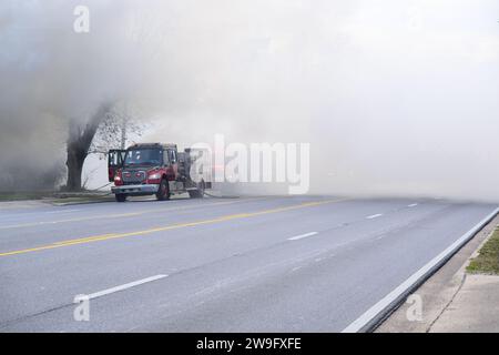 Au milieu d'un dense voile de fumée provenant d'un incendie voisin, un camion de pompiers rouge vif émerge comme un phare d'espoir et d'action. Le véhicule robuste se présente comme un sy Banque D'Images