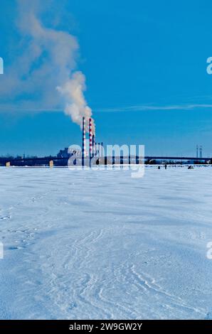 Une vieille centrale à charbon émission de fumée toxique dans l'atmosphère, paysage industriel urbain d'hiver avec rivière gelée Banque D'Images