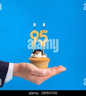 Main livrant cupcake d'anniversaire - bougie numéro 95 sur fond bleu Banque D'Images