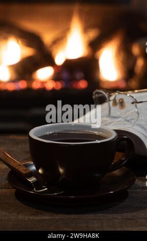 Tasse de café avec livre ouvert et couverture avec une cheminée brûlante en arrière-plan Banque D'Images