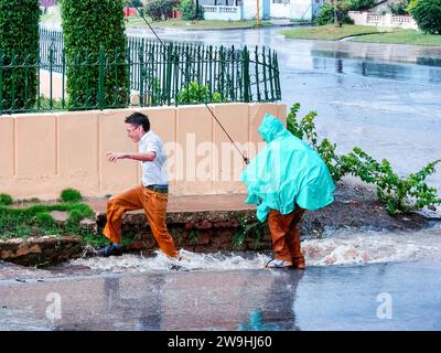 Étudiants en uniforme jouant dans l'eau de pluie dans une rue de la ville, Santa Clara, Cuba Banque D'Images