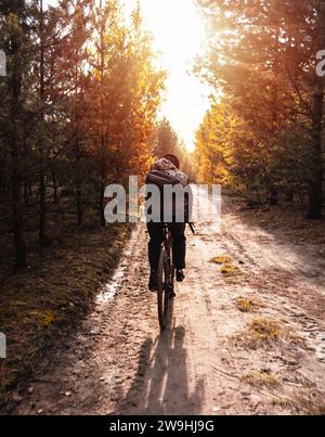 Jeune homme dans un casque monte un vélo de gravier sur un sentier dans la forêt d'automne au coucher du soleil. Mode de vie actif. Banque D'Images