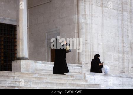 Deux femmes en burqas debout sur les marches devant la mosquée, prenant une photo avec leur téléphone portable. Istanbul, Turquie Banque D'Images