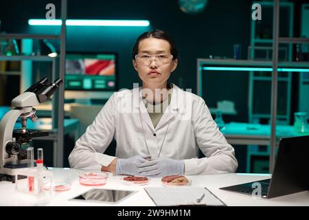 Jeune travailleuse asiatique de laboratoire assise sur son lieu de travail en laboratoire regardant la caméra Banque D'Images
