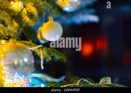 Plongez dans l'esprit des fêtes avec cette photo enchanteresse représentant des boules sur un sapin caucasien. Des lumières de Noël floues et un décor festif rehaussent le décor Banque D'Images