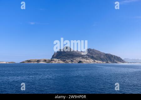 Une scène estivale tranquille prise depuis un ferry en route vers l'île Lofoten, représentant une montagne isolée et escarpée qui monte de la calme mer du Nord Banque D'Images