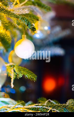 Plongez dans l'esprit des fêtes avec cette photo enchanteresse représentant des boules sur un sapin caucasien. Des lumières de Noël floues et un décor festif rehaussent le décor Banque D'Images