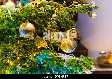 Des ornements suspendus illuminent un sapin de Noël, entouré par la lueur douce des lumières de Noël floues. Banque D'Images