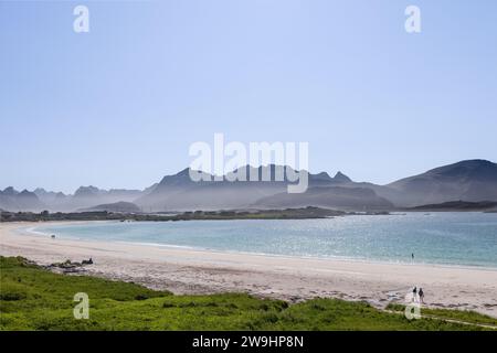 Les eaux scintillantes de la mer du Nord embrassent les rives de la plage Rambergstranda de la baie de Jusnesvika à Lofoten, en Norvège, avec une promenade de couples et un autre SWI Banque D'Images