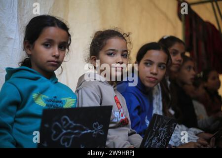 Rafah, Territoires palestiniens. 28 décembre 2023. Des enfants palestiniens écoutent leur professeur d’anglais Tariq al-Annabi (non représenté) alors qu’il continue à se permettre d’enseigner l’anglais aux enfants qui se sont réfugiés avec leur famille à l’école Abu Youssef Al-Najjar. Alors que la guerre contre Gaza se poursuit, les enfants poursuivent leur éducation dans des conditions difficiles en raison du manque de moyens éducatifs dans la bande de Gaza. Crédit : Mohammed Talatene/dpa/Alamy Live News Banque D'Images