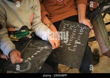 Rafah, Territoires palestiniens. 28 décembre 2023. Des enfants palestiniens écoutent leur professeur d’anglais Tariq al-Annabi (non représenté) alors qu’il continue à se permettre d’enseigner l’anglais aux enfants qui se sont réfugiés avec leur famille à l’école Abu Youssef Al-Najjar. Alors que la guerre contre Gaza se poursuit, les enfants poursuivent leur éducation dans des conditions difficiles en raison du manque de moyens éducatifs dans la bande de Gaza. Crédit : Mohammed Talatene/dpa/Alamy Live News Banque D'Images