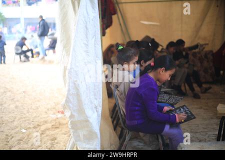 Rafah, Territoires palestiniens. 28 décembre 2023. Des enfants palestiniens écoutent leur professeur d’anglais Tariq al-Annabi (non représenté) alors qu’il continue à se permettre d’enseigner l’anglais aux enfants qui se sont réfugiés avec leur famille à l’école Abu Youssef Al-Najjar. Alors que la guerre contre Gaza se poursuit, les enfants poursuivent leur éducation dans des conditions difficiles en raison du manque de moyens éducatifs dans la bande de Gaza. Crédit : Mohammed Talatene/dpa/Alamy Live News Banque D'Images