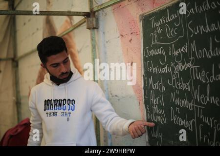 Rafah, Territoires palestiniens. 28 décembre 2023. Le professeur palestinien d'anglais Tariq al-Annabi continue d'enseigner l'anglais aux enfants qui se sont réfugiés avec leur famille à l'école Abu Youssef Al-Najjar. Alors que la guerre contre Gaza se poursuit, les enfants poursuivent leur éducation dans des conditions difficiles en raison du manque de moyens éducatifs dans la bande de Gaza. Crédit : Mohammed Talatene/dpa/Alamy Live News Banque D'Images