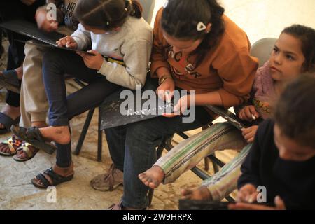 Rafah, Territoires palestiniens. 28 décembre 2023. Des enfants palestiniens écoutent leur professeur d’anglais Tariq al-Annabi (non représenté) alors qu’il continue à se permettre d’enseigner l’anglais aux enfants qui se sont réfugiés avec leur famille à l’école Abu Youssef Al-Najjar. Alors que la guerre contre Gaza se poursuit, les enfants poursuivent leur éducation dans des conditions difficiles en raison du manque de moyens éducatifs dans la bande de Gaza. Crédit : Mohammed Talatene/dpa/Alamy Live News Banque D'Images