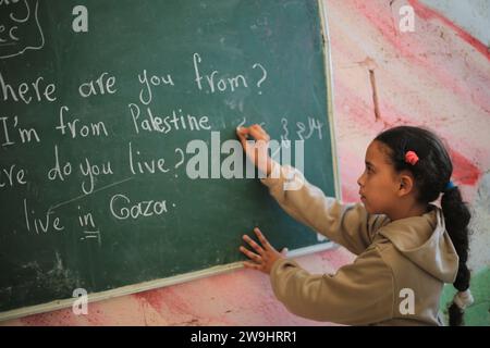 Rafah, Territoires palestiniens. 28 décembre 2023. Une jeune fille palestinienne écoute son professeur d'anglais Tariq al-Annabi (non représenté) alors qu'il continue à se permettre d'enseigner l'anglais aux enfants qui se sont réfugiés avec leur famille à l'école Abu Youssef Al-Najjar. Alors que la guerre contre Gaza se poursuit, les enfants poursuivent leur éducation dans des conditions difficiles en raison du manque de moyens éducatifs dans la bande de Gaza. Crédit : Mohammed Talatene/dpa/Alamy Live News Banque D'Images