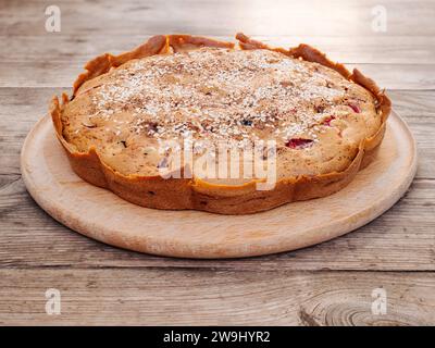 Tarte aux cerises maison rustique fraîchement cuite et aux prunes parsemée de graines de sésame sur une planche à découper ronde sur une vieille table en bois. Style campagnard Banque D'Images