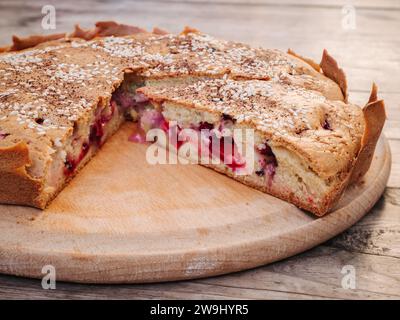 Rustique maison cerise et tarte aux prunes aux cerises parsemée de graines de sésame sur une planche à découper ronde sur une vieille table en bois en gros plan. Style campagnard Banque D'Images