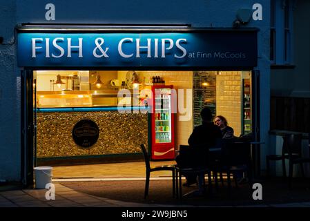 Magasin Fish and Chips la nuit photographié de l'extérieur regardant à l'intérieur des restaurants mangeant du Fish and Chips. Teignmouth, Devon, Angleterre. Banque D'Images