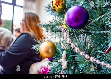 Un sapin de Noël décoré de boules colorées avec une dame assise en arrière-plan Banque D'Images