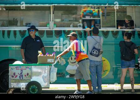 Un vendeur de crème glacée gère son chariot de poussée comme un camion de tacos sert des clients multiethniques lors d'un festival dans un parc à Santa Ana, CA. Banque D'Images