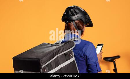 Cycliste attendant que la commande soit traitée avant de récupérer le repas pour la commission à venir. Courrier vérifiant l'application de téléphone pour trouver l'emplacement de la prochaine maison du client, isolé sur fond de studio, gros plan Banque D'Images