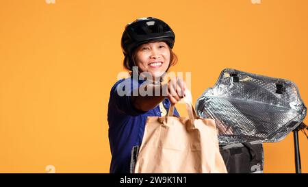 Gros plan du coursier arrivant à l'adresse du client, sortant le sac de repas du sac à dos thermique. Heureux pilote de vélo BIPOC livrant le déjeuner au client, isolé sur fond de studio Banque D'Images