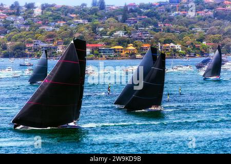 Voiles noires de maxi yachts après la ligne de départ sur le port de Sydney dans une course vers Hobart, Australie. Banque D'Images