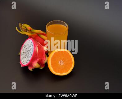 Un grand verre de jus de fruits jaunes sur fond noir, à côté d'orange mûre et de fruits pitaya. Gros plan. Banque D'Images