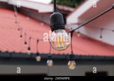 Une petite ampoule LED en forme de globe de style Edison qui a des filaments de couleur orange et du verre ambré clair. Ceci est une ampoule de corde de décoration extérieure Banque D'Images