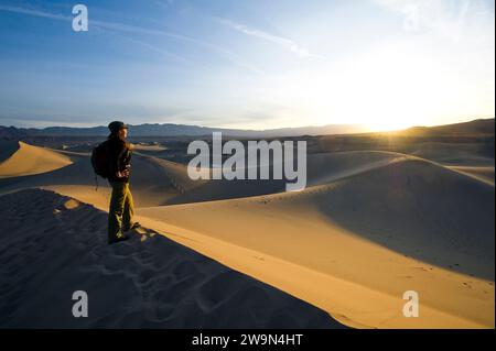 Une jeune femme regarde le lever du soleil depuis les dunes de sable plates de Mesquite dans le parc national de la Vallée de la mort, en Californie. Banque D'Images