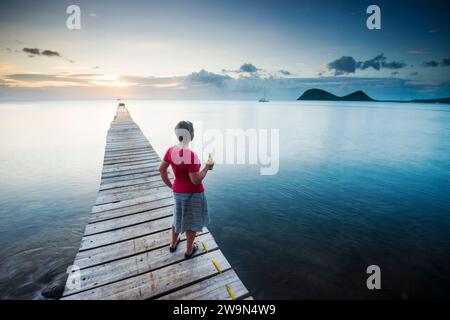 Une femme profite du coucher de soleil sur la mer des Caraïbes sur un quai de l'hôtel Portsmouth Beach dans la ville de Portsmouth sur l'île de la Dominique. Banque D'Images