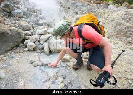 Une femme sent la chaleur se dégager des piscines chaudes de sulfer dans la vallée de la Désolation sur son chemin vers le lac Boiling sur l'île caribéenne de la Dominique. Banque D'Images