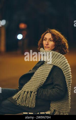 pensive femme d'âge moyen assise sur une chaise dans la ville de nuit Banque D'Images